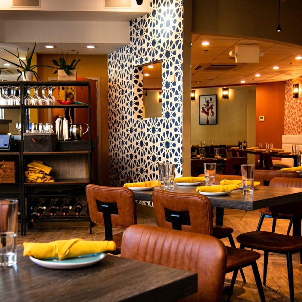 Restaurant interior with tables set with yellow napkins, brown chairs, and a patterned wall.