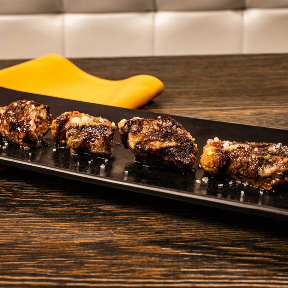 Four pieces of grilled meat with salt flakes on a black rectangular plate, with a yellow napkin.